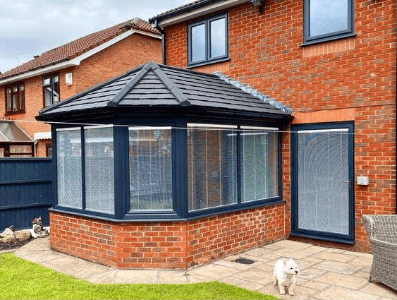 Grey tiled conservatory roof replacement on red brick home with large windows